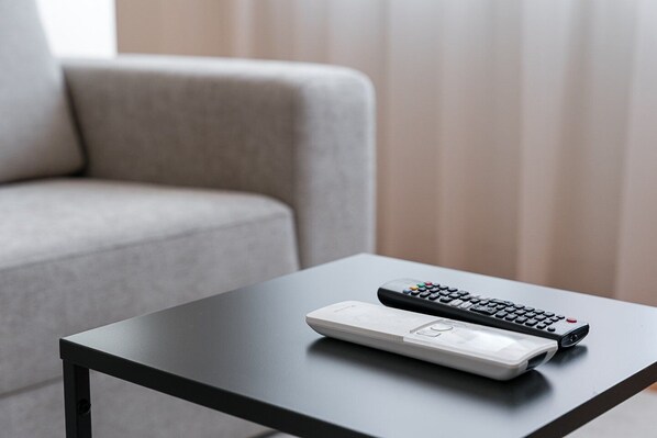 A remote control and a white device on a black table in a room with a grey sofa.