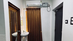 A bathroom with a wooden door, a sink, a shower, and a dark floor. - HOTEL N N PALACE (Thanjavur)