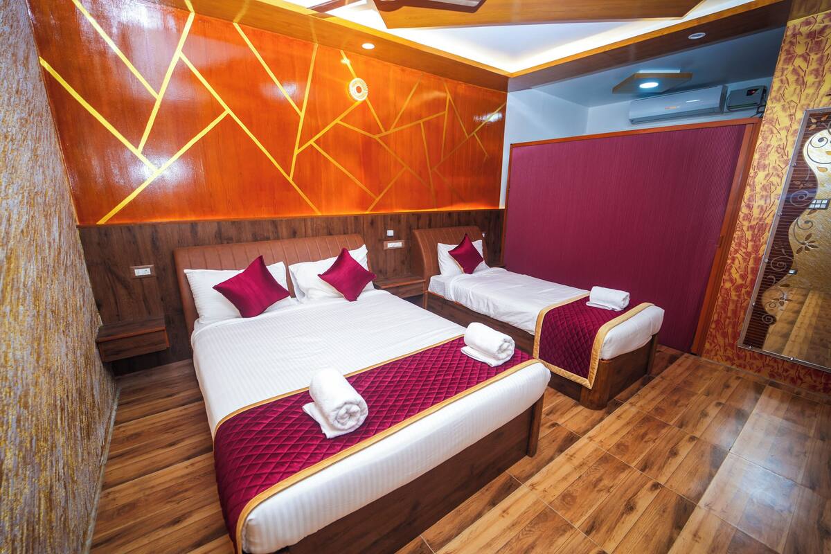 A hotel room with two beds, wooden flooring, and a red accent wall.