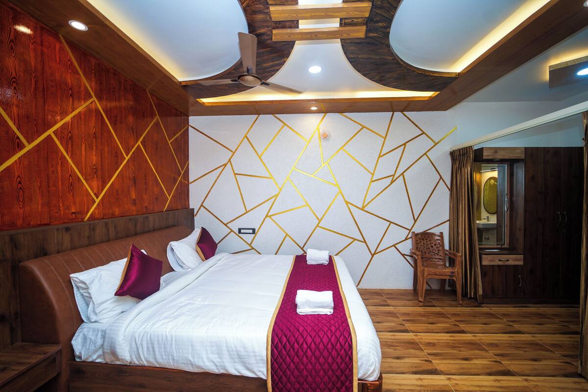 A well-lit bedroom with a wooden ceiling, a bed with white bedding and a red blanket, and a geometric wall design.