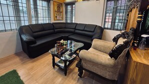 A living room with a black sectional sofa, a glass coffee table, and a wooden chair. - HOTEL N N PALACE (Thanjavur)