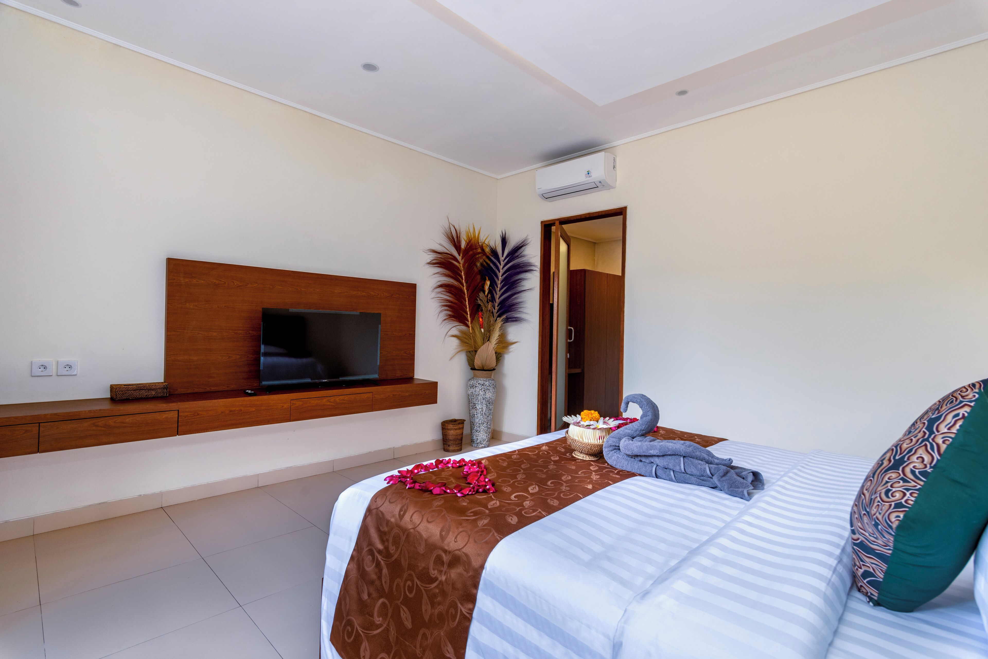 Ein modernes Hotelzimmer mit einem großen Bett, einem wandmontierten Flachbildfernseher, einer Vase mit Trockenpflanzen und einem kleinen Tisch mit Blumenarrangements.