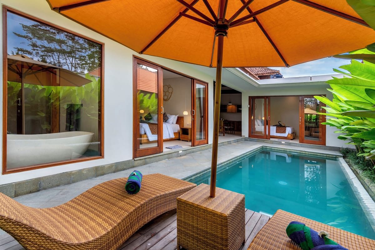 A poolside area with wicker furniture, an umbrella, and a view of the pool and adjacent rooms.