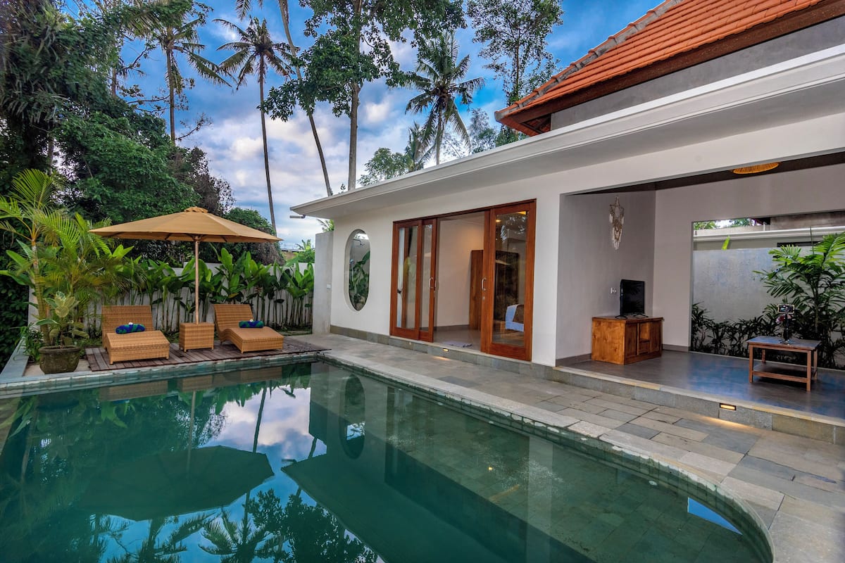 A modern house with a swimming pool, wooden deck, and tropical plants.