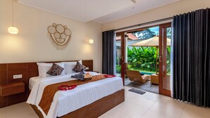 Een ruime slaapkamer met een groot bed, een houten hoofdbord en uitzicht op een weelderige tuin door een schuifdeur van glas.