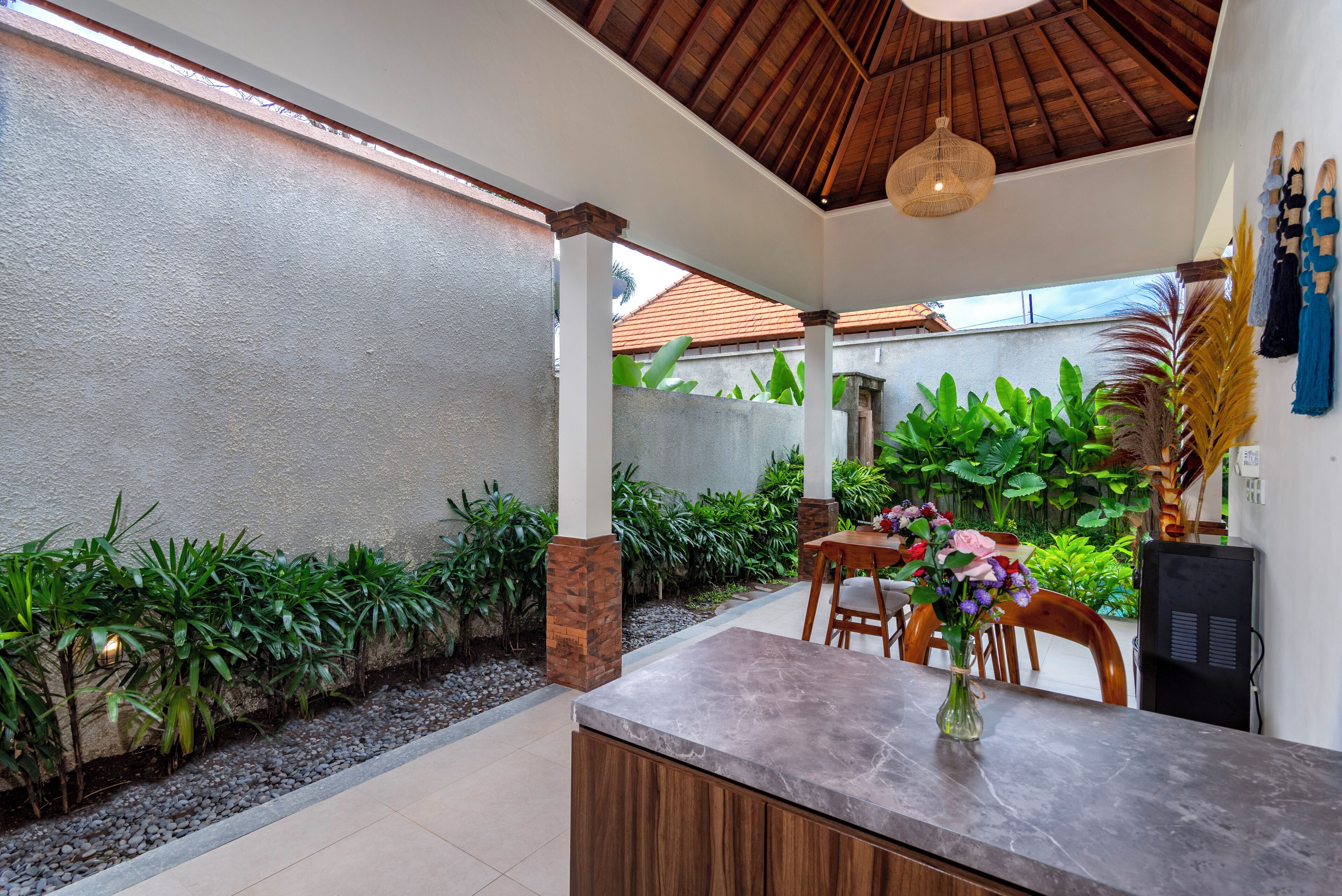 Un área de comedor al aire libre moderna con pared de piedra, follaje y una mesa de madera con sillas.