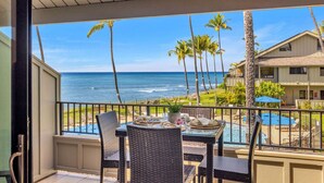 A balcony with a view of the ocean, a pool, and palm trees.