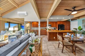 Amplia sala de estar con sofá, mesa de comedor y sillas, cocina con armarios de madera y ventilador de techo.