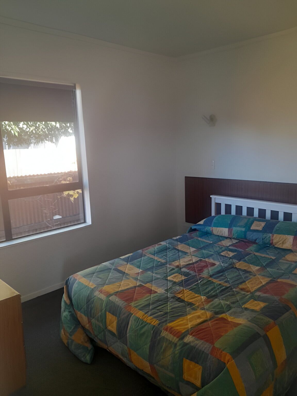 Un dormitorio con cama, ventana y mesita de noche.
