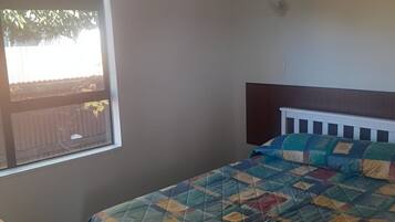 Un dormitorio con cama, ventana y mesita de noche.