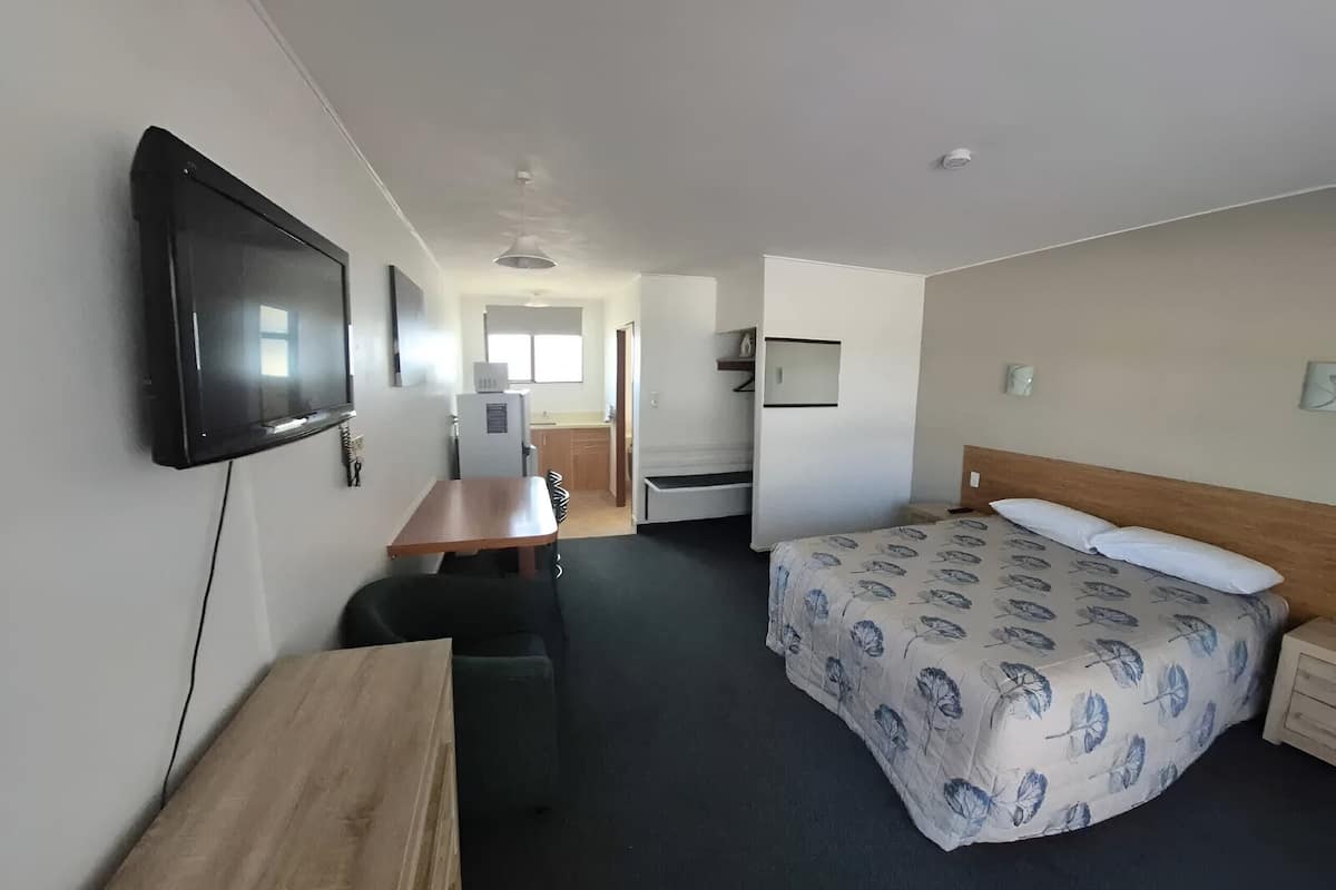 Una habitación de hotel con una cama, un escritorio, una silla, un televisor y una kitchenette.
