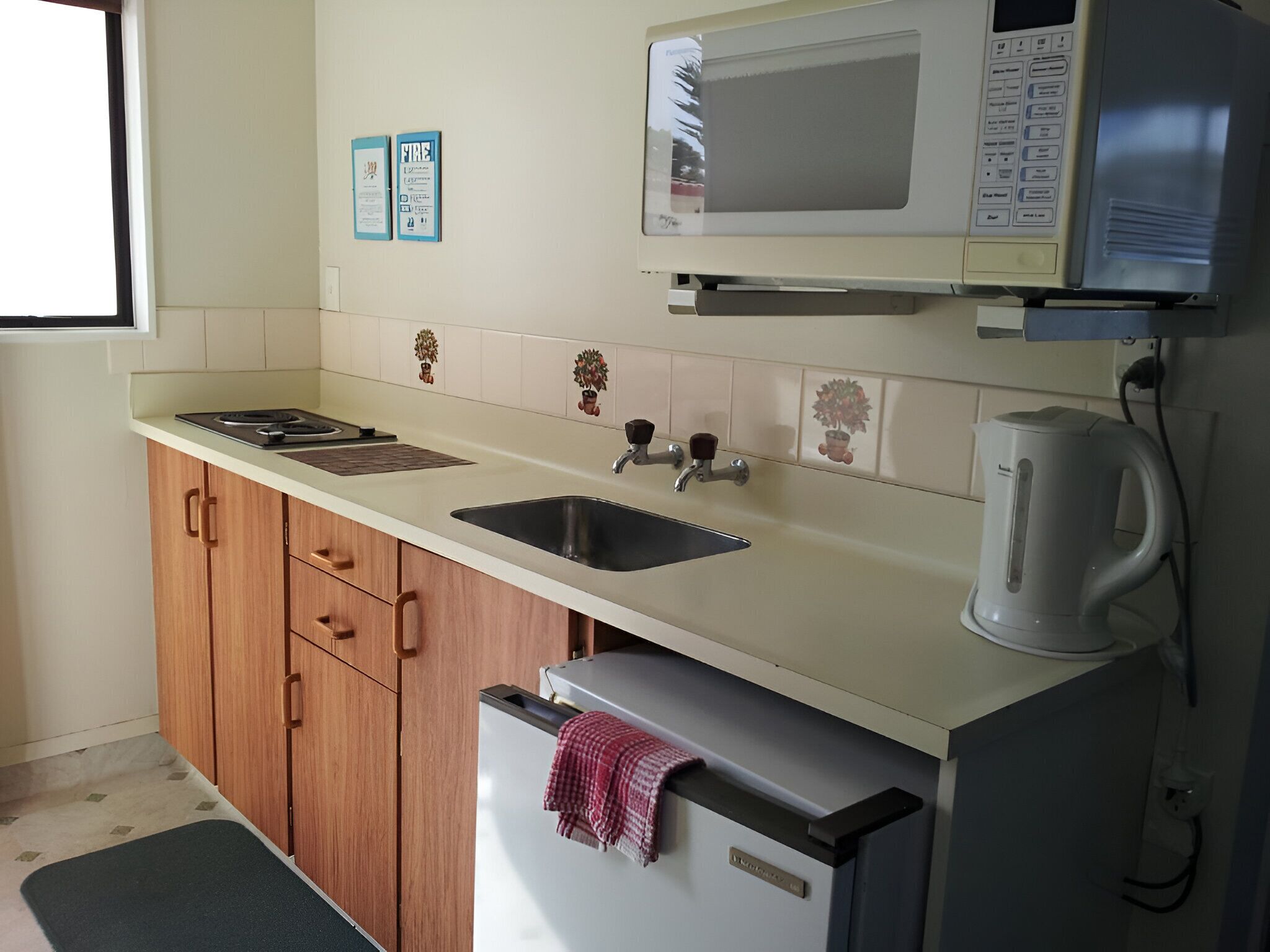 Een keuken met een magnetron, spoelbak, kastjes en een waterkoker.