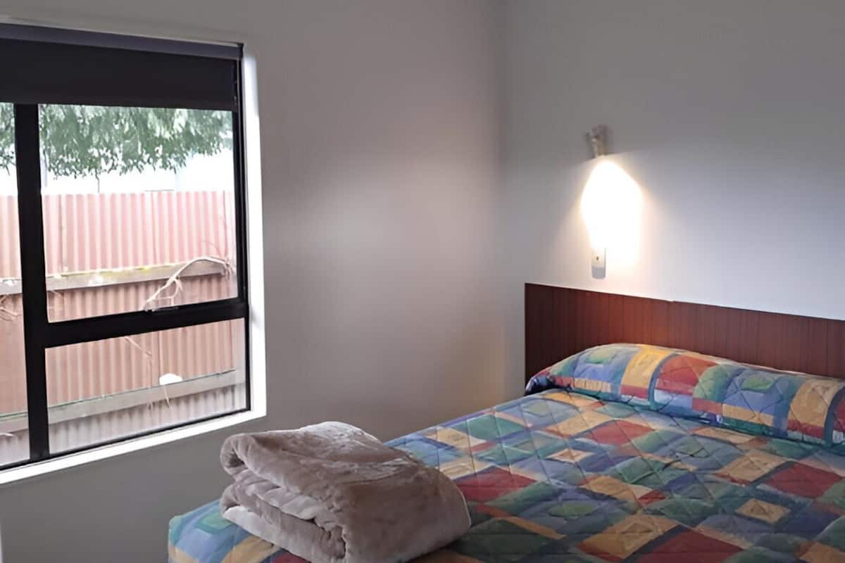 Habitación de hotel con cama, ventana y lámpara de pared.