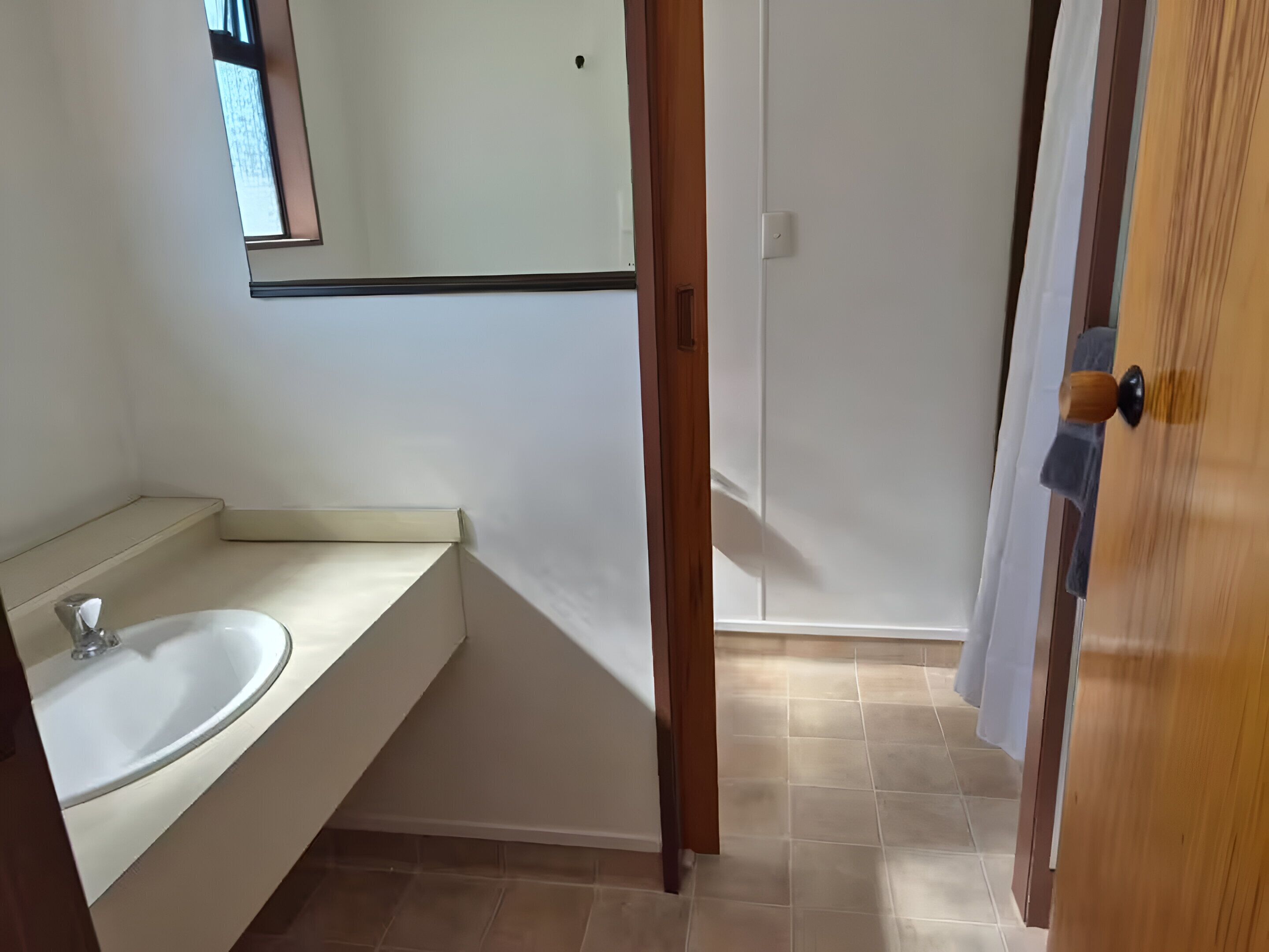Een badkamer met een wastafel, spiegel en een deur naar een andere kamer.