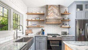 Eine Küche mit weißen, in Ziegeloptik angeordneten Fliesen, Holzböden, einem Edelstahlkühlschrank und einem eingebauten Backofen.