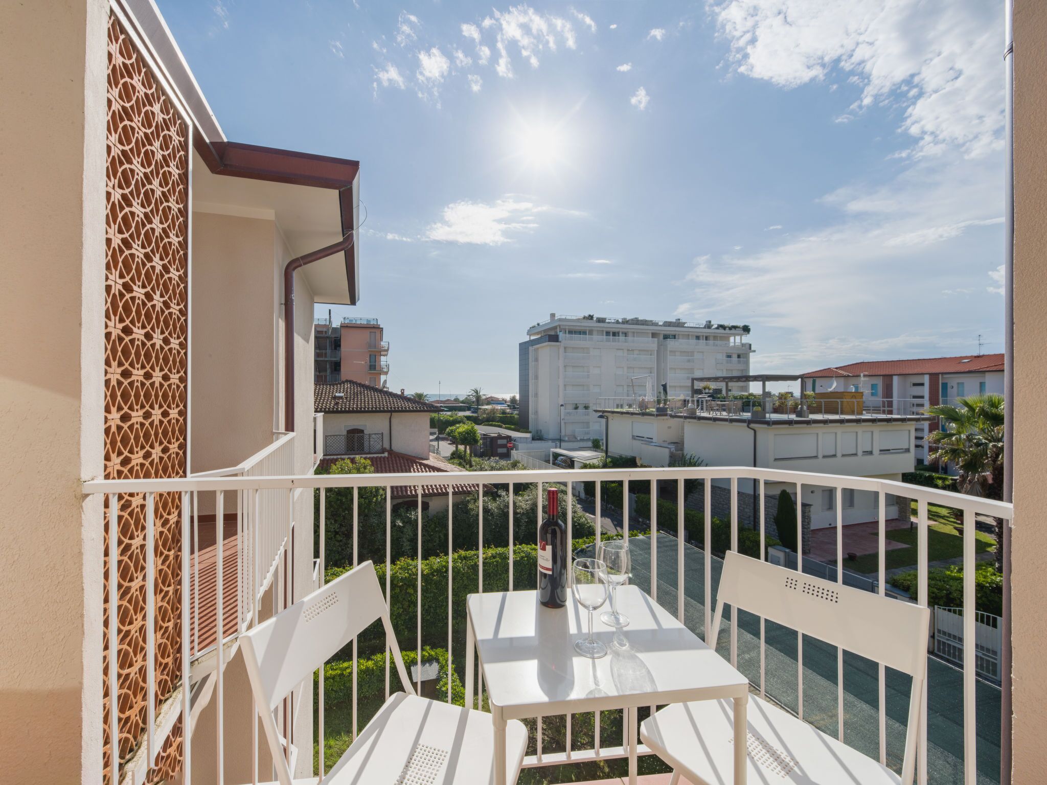 Un balcón con una mesa y sillas blancas, con vistas a una zona residencial con edificios y vegetación.