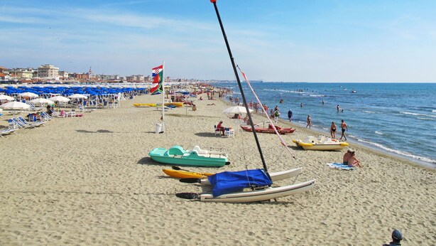 Una playa con kayaks, canoas, una bandera y sombrillas.