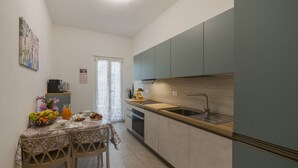 Cocina compacta con comedor, que incluye un lavamanos, armarios y una mesa servida con frutas y una jarrón.