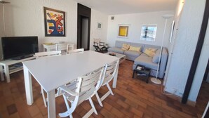 A modern living room with a white dining table, grey sofa, and a television.