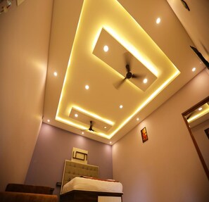 Une chambre d’hôtel dotée d’un plafond au design moderne, avec des luminaires encastrés et un ventilateur au centre.
