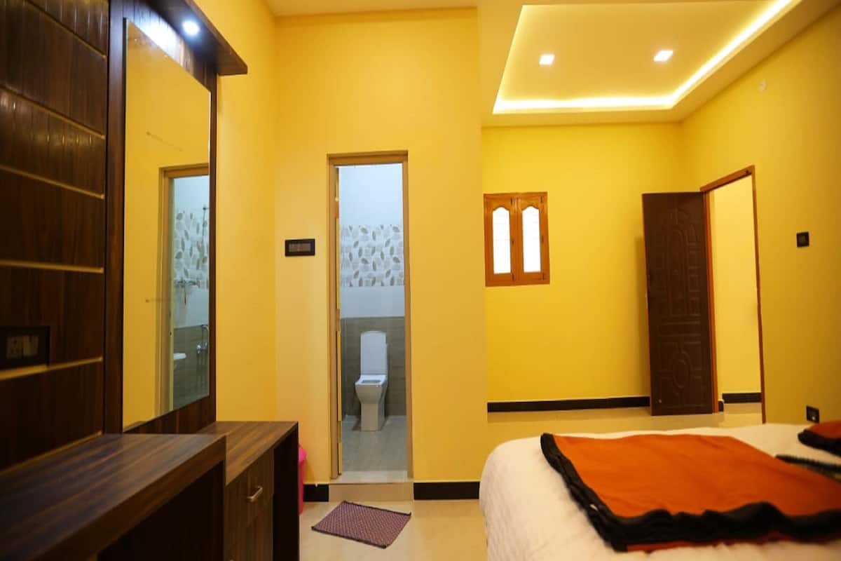 A bedroom with a bed, a wooden wardrobe, a bathroom with a toilet, and a mirror.