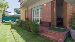 Ein zweistöckiges Haus mit Balkon, Eingangstür und kleinem Vorgarten mit Rasen und Stuhl.