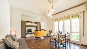 Ein modernes Wohnzimmer mit einer Couch, einem Esstisch und Stühlen. Es gibt eine Küchenzeile mit einem Fernseher und Schränken.