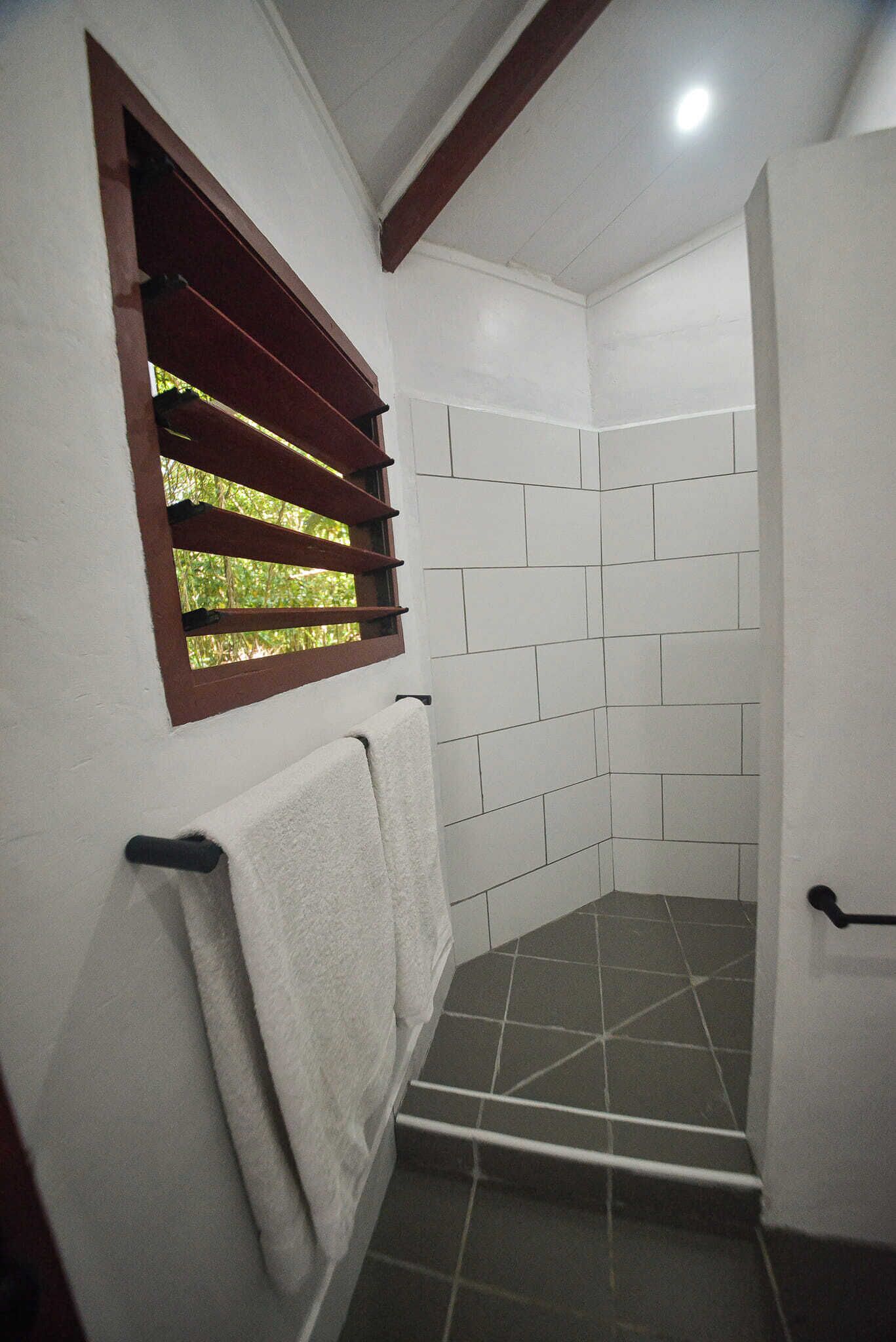 A bathroom with white tiled walls, a window with brown blinds, and a towel hanging on a rack.