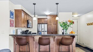 A modern kitchen with wooden cabinets, stainless steel appliances, and a bar area with stools.