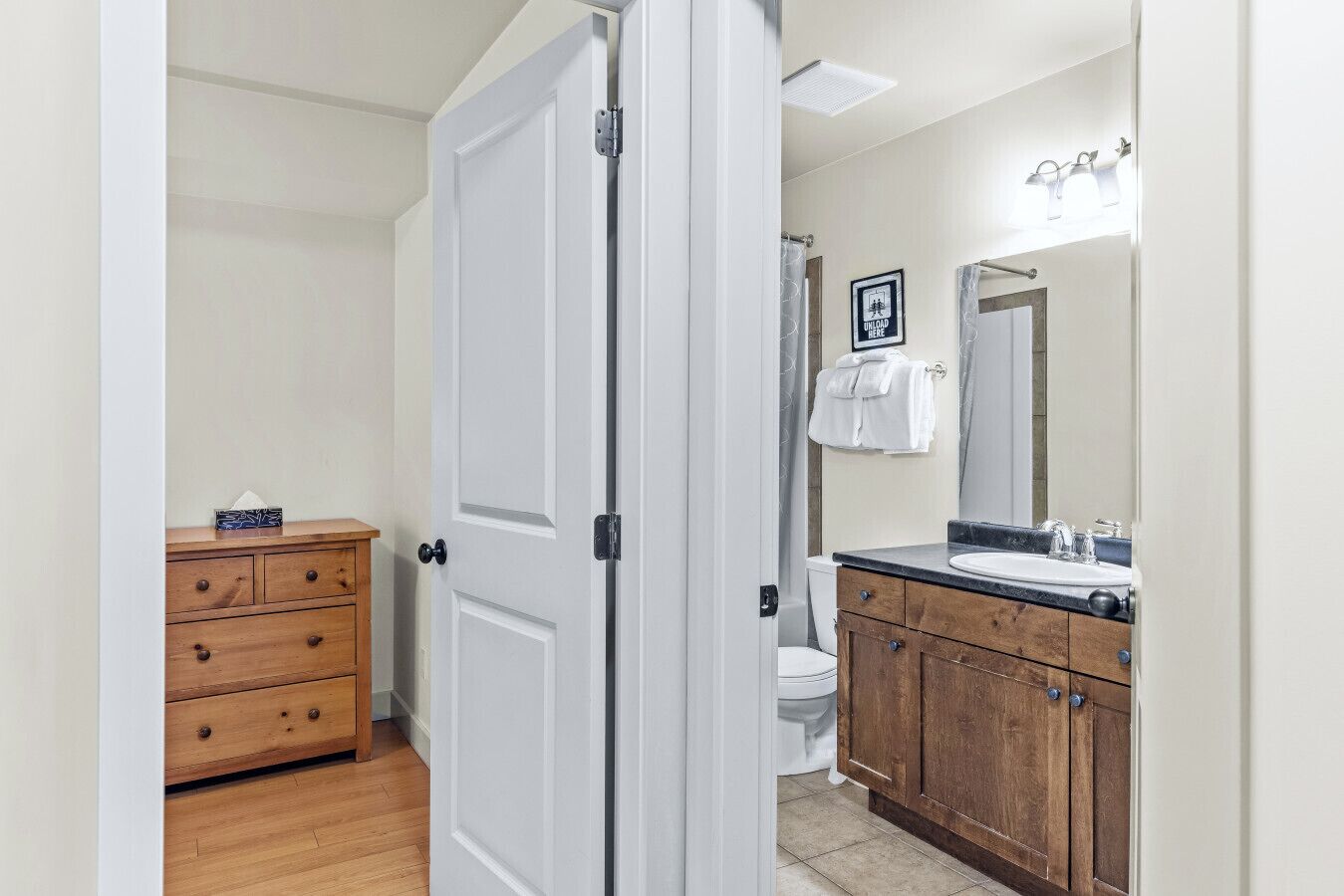 Une salle de bain avec des toilettes blanches, un lavabo et un miroir. On y trouve un meuble en bois avec des tiroirs, et une serviette est accrochée au mur.