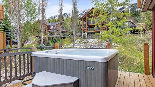 A hot tub on a wooden deck with a view of a mountain and lodge buildings.