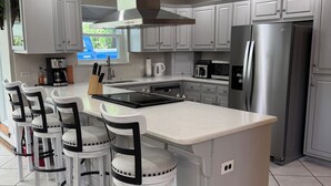 Una cocina moderna con una isla central, taburetes de bar, electrodomésticos de acero inoxidable y armarios blancos.