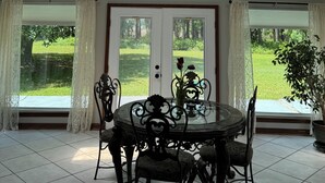 Un solárium con techo inclinado, tragaluces, una mesa de comedor con sillas y vista a un paisaje verde.