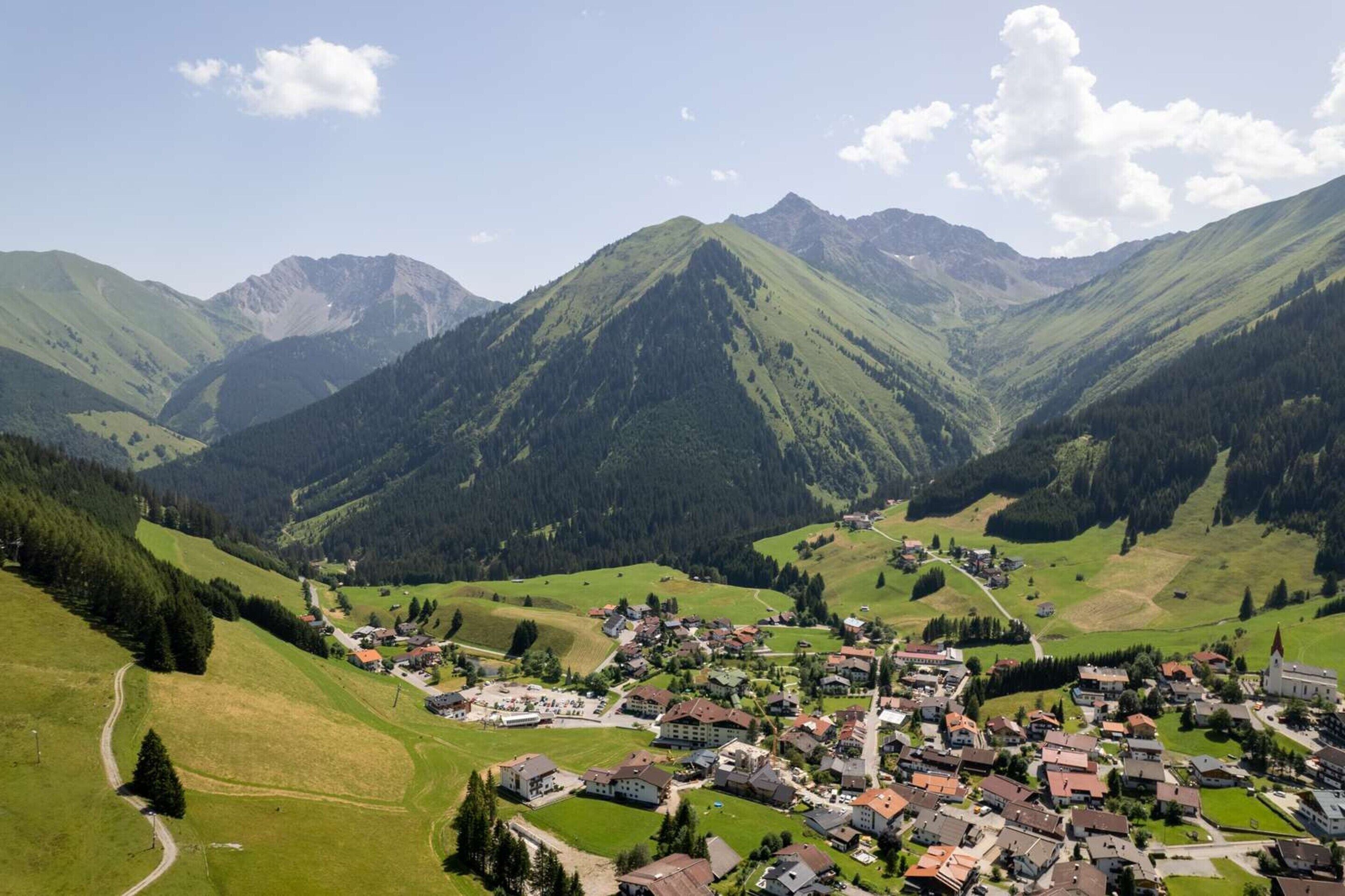 A mountainous village with a central church, surrounded by lush green hills and a clear sky.