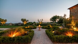 Un sendero en un jardín que conduce a una fuente central, rodeada de setos y árboles podados.