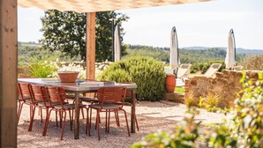 Un patio al aire libre con una mesa y sillas, rodeado por un muro de piedra y vistas al campo.