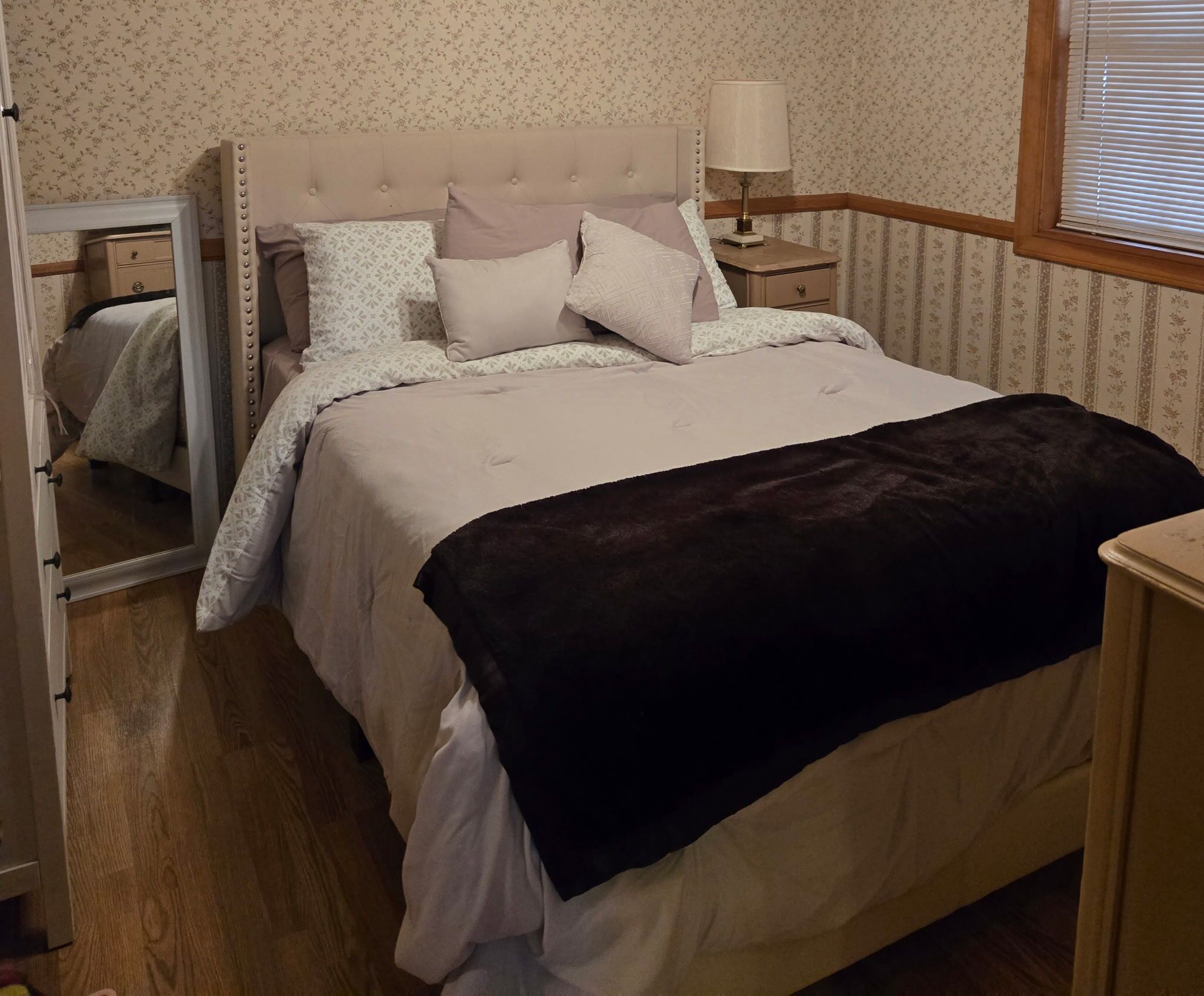 Un lit bien fait, avec une tête de lit, une lampe de chevet et un miroir accroché au mur.