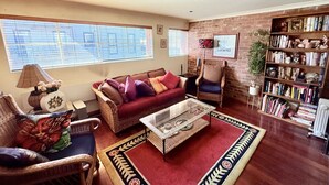 A living room with a red sofa, a glass coffee table, wicker chairs, a bookshelf, and a brick wall.