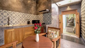 A dining area with a round wooden table, a white vase with red flowers, and a patterned wall. - Lanturan Ubud-Villas (Ubud)