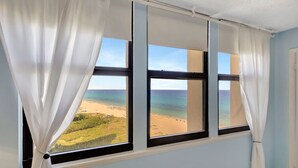 Ein Zimmer mit großem Fenster und Blick auf Strand und Meer.