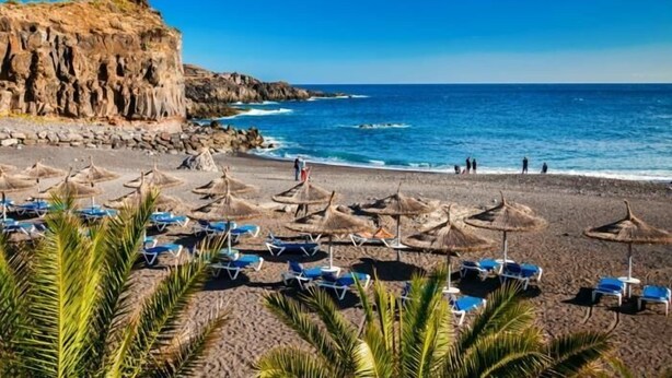 A beach with umbrellas and lounge chairs, rocky cliffs, and the ocean. - Exclusive Villa Olivia with Private heated Pool (Callao Salvaje)