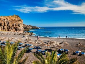 Una platja amb ombrelles i gandules, penya-segats rocosos i l'oceà.