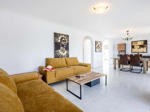 A modern living room with a sofa, a coffee table, and a dining area with chairs and a table.