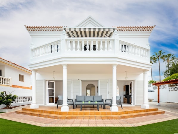 A two-story white house with a covered porch, a balcony, and a well-maintained lawn.