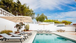 A swimming pool with lounge chairs and umbrellas, surrounded by a white wall and greenery. - Exclusive Villa Olivia with Private heated Pool (Callao Salvaje)