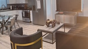A modern kitchen with white cabinets, a stainless steel refrigerator, and a microwave. There is a dining area with a glass table and chairs. - Charming 2-bedroom house in Azusa with WiFi and AC (Azusa)