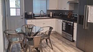 A modern kitchen with white cabinets, stainless steel appliances, a glass dining table, and a window with blinds. - Charming 2-bedroom house in Azusa with WiFi and AC (Azusa)