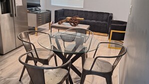 A modern kitchen with a built-in refrigerator, a dining area with a glass table and metal chairs, and a dark-colored sofa in the background. - Charming 2-bedroom house in Azusa with WiFi and AC (Azusa)