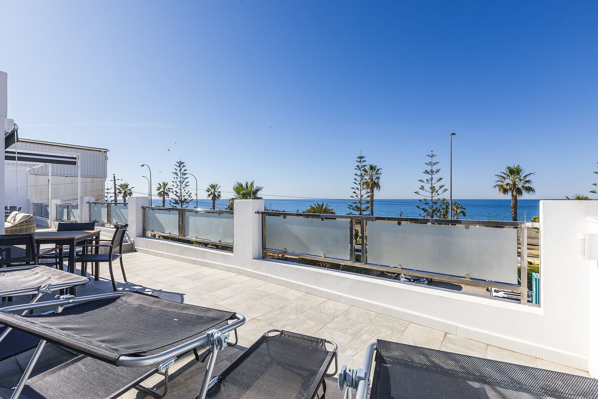 A rooftop terrace with outdoor seating, a view of the sea, and palm trees.
