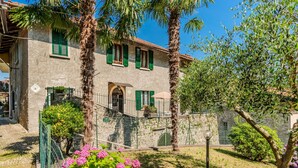A two-story building with a stone facade, green shutters, and a small balcony.